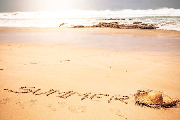 Photo touristic hat on the sand and word summer written