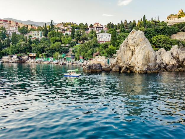 Touristic small catamaran passing by the rock cliff coast on the sea