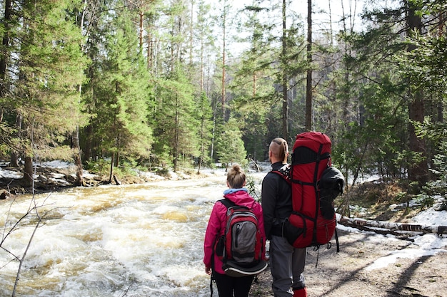 Туристы - парень и девушка смотрят на горную реку в лесу