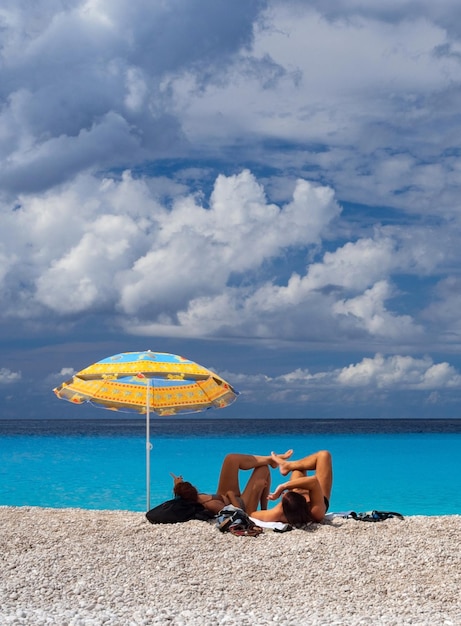 Tourists under a beach umbrella on a sunny day in Ionian Sea on the island of Kefalonia in Greece