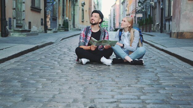 観光客は、舗装の上に座って歴史的な環境を眺めながら地図をカップルします。彼らは興奮して微笑んでいます。