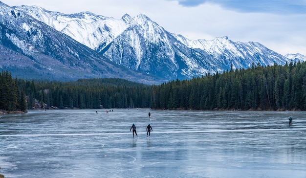 冬のバンフ国立公園のジョンソン湖の凍った水面でアイススケートをしている観光客