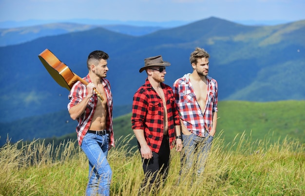 Tourists hiking concept Hiking with friends Long route Adventurers squad Group of young people in checkered shirts walking together on top of mountain Men with guitar hiking on sunny day