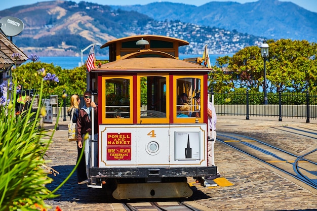 Foto turisti con il bianco sul tram su una strada piatta con la baia di san francisco e le montagne