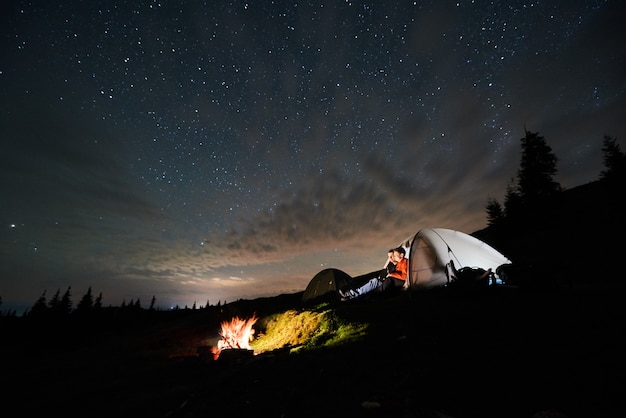 写真 キャンプファイヤーと夜の星空の下でテントの近くの観光客