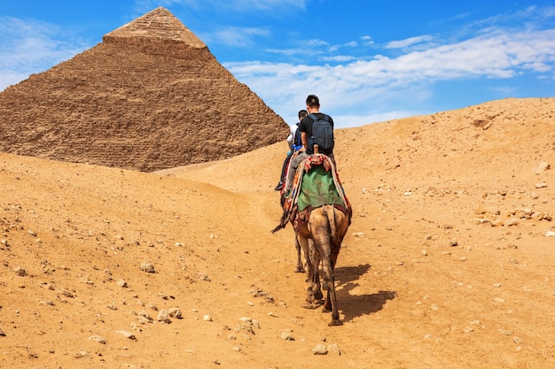 기자 카프레의 피라미드 근처에서 낙타를 타고 있는 관광객들.