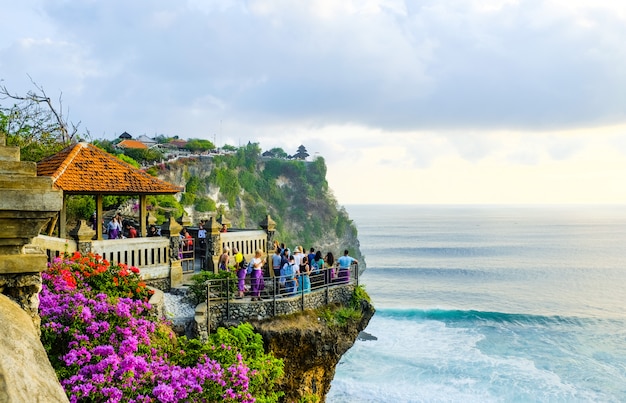 Tourists stand at sunset and admire the scenery on a cliff near the Uluwatu Temple on the island of Bali, Indonesia