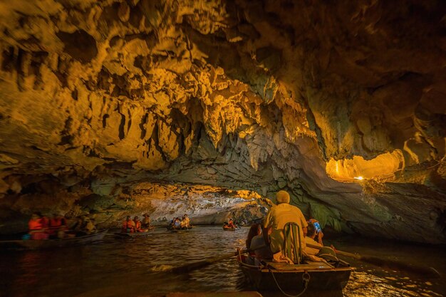 Tourists traveling in boats along the Ngo Dong River at the Tam Coc portion Ninh Binh Province Vietnam Rowers using their feet to propel oars Landscape formed by karst towers and rice fields