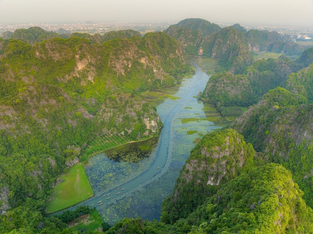 Tourists traveling in boats along the Ngo Dong River at the Tam Coc portion Ninh Binh Province Vietnam Rowers using their feet to propel oars Landscape formed by karst towers and rice fields