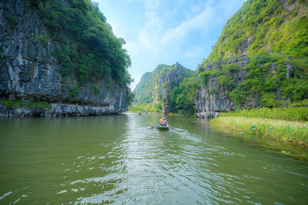 Tourists traveling in boats along the Ngo Dong River at the Tam Coc portion Ninh Binh Province Vietnam Rowers using their feet to propel oars Landscape formed by karst towers and rice fields