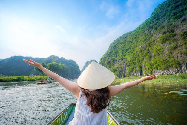 Tourists traveling in boats along the Ngo Dong River at the Tam Coc portion Ninh Binh Province Vietnam Rowers using their feet to propel oars Landscape formed by karst towers and rice fields