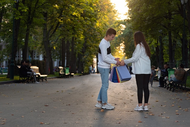 Туристы гуляют в осеннем парке с бумажными хозяйственными пакетами.