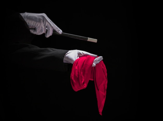 Tovenaar die truc op rood servet met toverstokje uitvoeren tegen zwarte achtergrond
