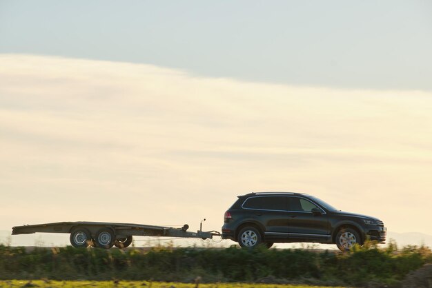 Tow truck vehicle with car transporting carrier trailer driving on highway in evening.