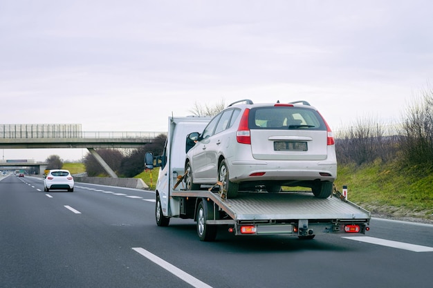 Tow truck with car on warranty on road. Trailer and crash auto delivery. Vehicles hauler on driveway. European transport logistics. Heavy haul trailer with driver on highway.