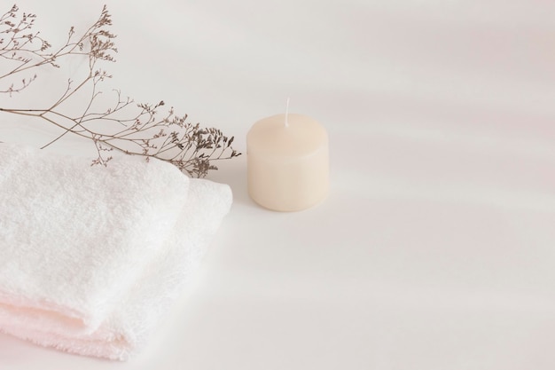 Свеча-полотенце и сушеные полевые цветы на белом столе Теплый свет и тени