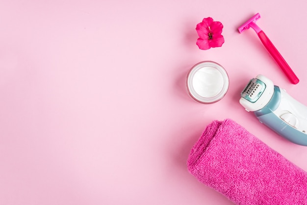 Towel, cream, razor and flower on pink background. Flat lay. Skincare.