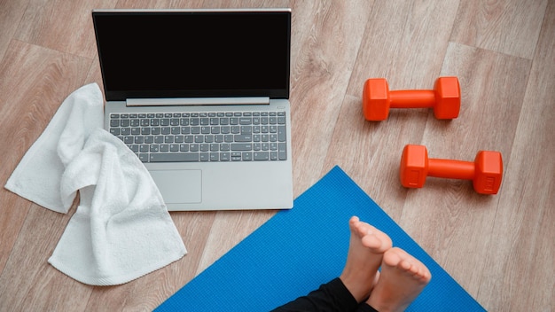 Foto asciugamano manubri laptop vista dall'alto giovane donna fare esercizi di allungamento fitness allenamento utilizzando il laptop donna in abbigliamento sportivo fare yoga esercizio yoga a distanza lezione di yoga seduto durante il soggiorno a casa banner web lungo