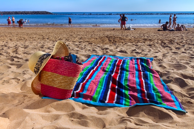 Towel and straw bag on beach by the ocean