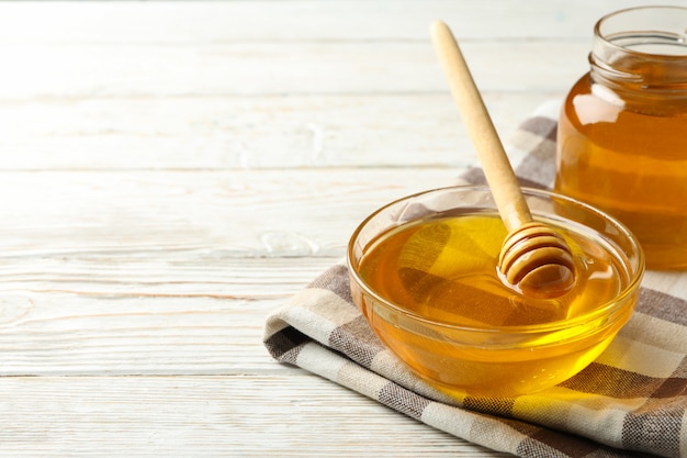 Towel with bowl and jar of honey and dipper on white wooden background