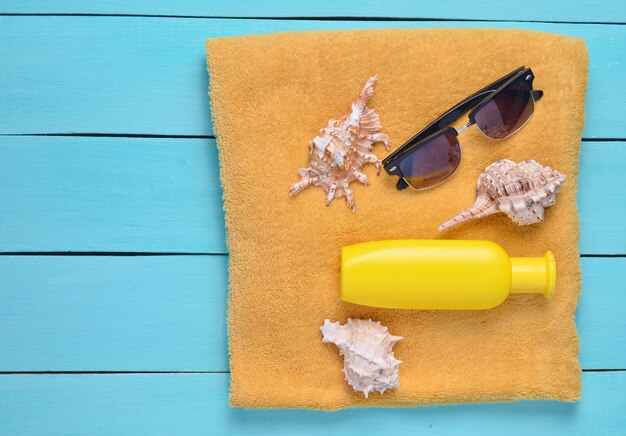 Towel with sunscreen, cockleshells, sunglasses on blue wooden boards