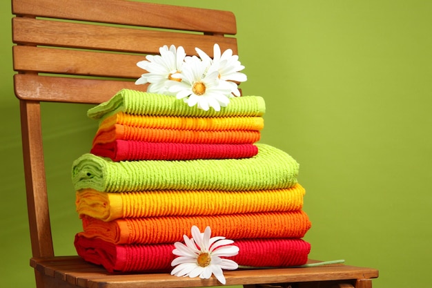 Towels and flowers on wooden chair on green background