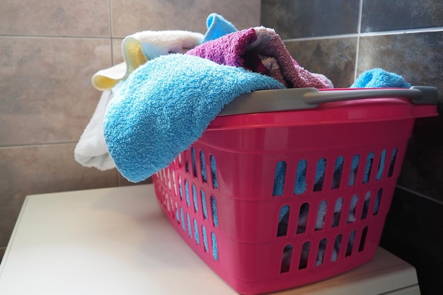 Towels in the laundry basket blue and pink cotton terry towels\
are thrown into a pink plastic basket housekeeping storing and\
separating laundry before washing light from above from open\
window