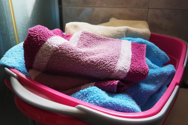 Towels in the laundry basket blue and pink cotton terry towels\
are thrown into a pink plastic basket housekeeping storing and\
separating laundry before washing light from above from open\
window