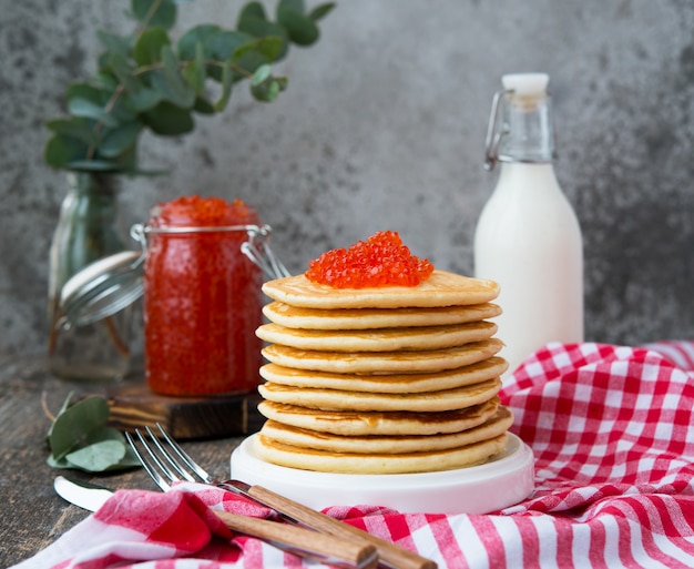 Una torre di pancake americano con caviale rosso si erge su uno sfondo grigio di legno.