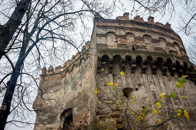 The tower of the ancient fortress in Ostrog, Ukraine, close-up. Late autumn.  Yellow leaves on the branches of the trees