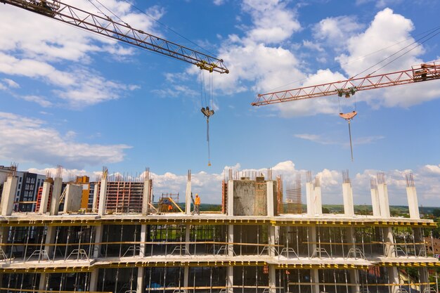 Tower crane at high concrete residential building under construction. Real estate development concept.