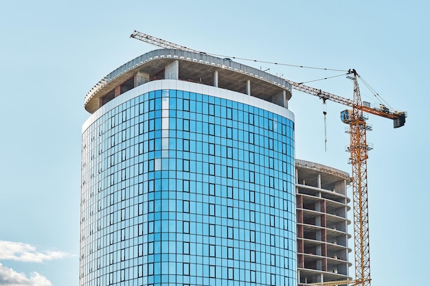 Tower crane near contemporary skyscraper with shiny glass facade at construction site against sky