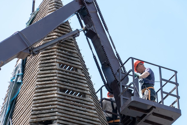 A tower crane with a cradle lifts people to perform work on\
repairing the roof of the old historical knowledge replacement of\
roof tiles performing installation work at height