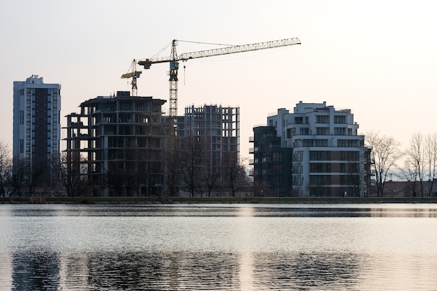 Tower cranes and high residential apartment buildings under construction on lake shore. Real estate development.