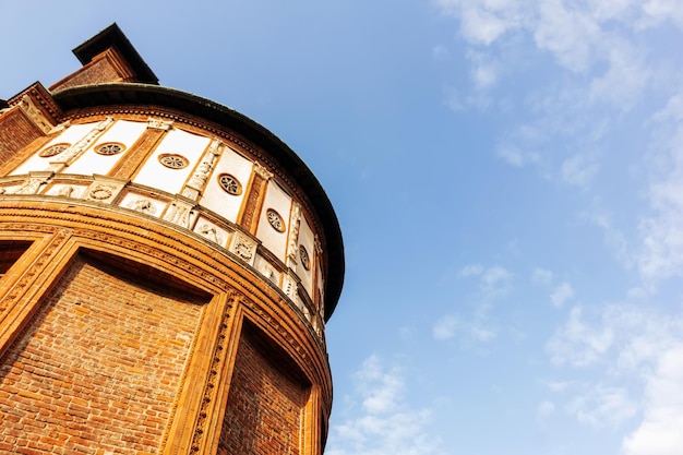 A tower of red and yellow bricks against a pale blue sky and white clouds