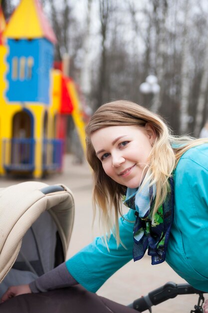 Town walk with stroller young active mother in blue trench coat walking on playground with her baby in pram