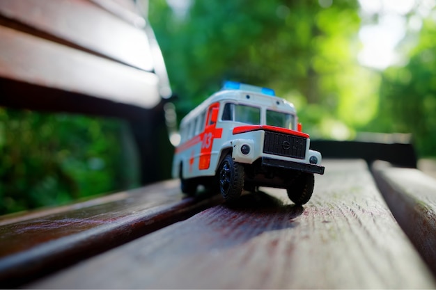 Фото Игрушечная машина скорой помощи на скамейке в парке на фоне боке