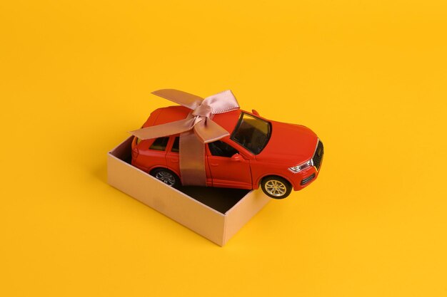 Photo toy auto model rewound gift ribbon with bow in box on yellow background car as gift surprise