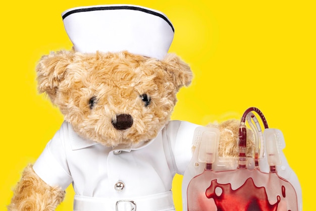 A toy bear in nurse uniform holding a blood bag. Blood donation concept.