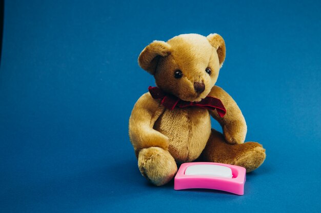 Toy bear sits with toy soap on a blue background.