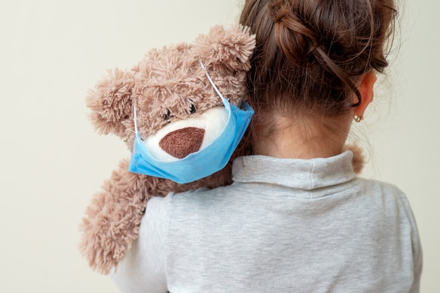 Toy bear with protective mask on child shoulder