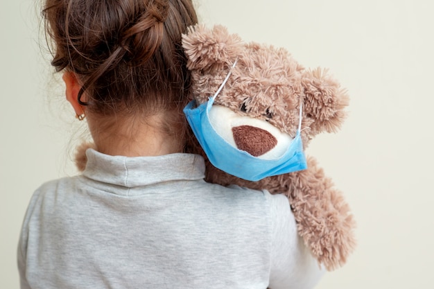 Toy bear with protective mask on child shoulder