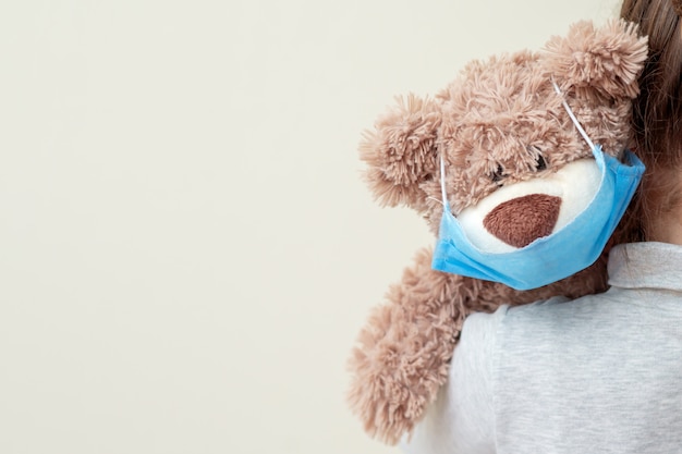 Toy bear with protective mask on child shoulder