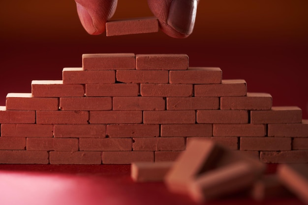 Photo toy block hand holding small red brick building a wall