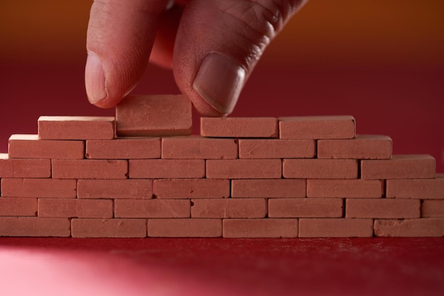 Foto mano di blocco giocattolo che tiene un piccolo mattone rosso che costruisce un muro