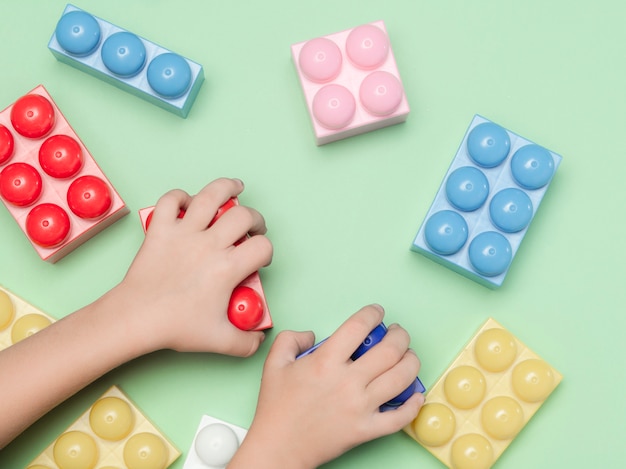 Toy blocks. Child is playing with colorful constructor bricks. Educational toy, flat lay, top view.