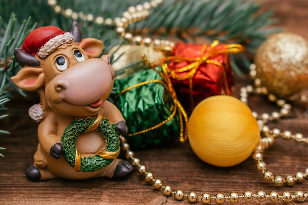 Toy bull in a Santa Claus hat.Christmas tree branch with little gift boxes and balls.