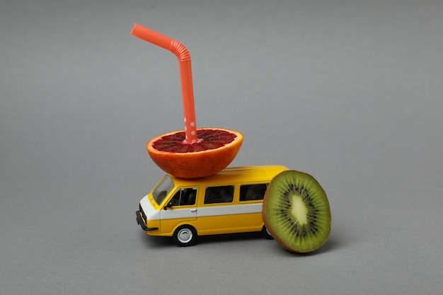 Toy bus with fruits and straw on gray isolated background