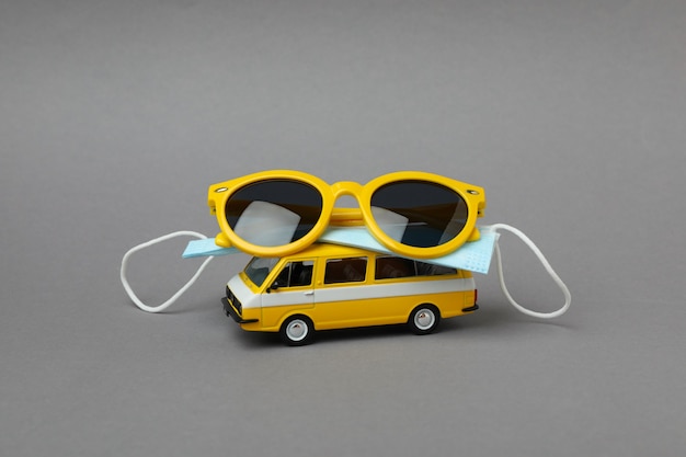 Toy bus with sunglasses and mask on gray isolated background