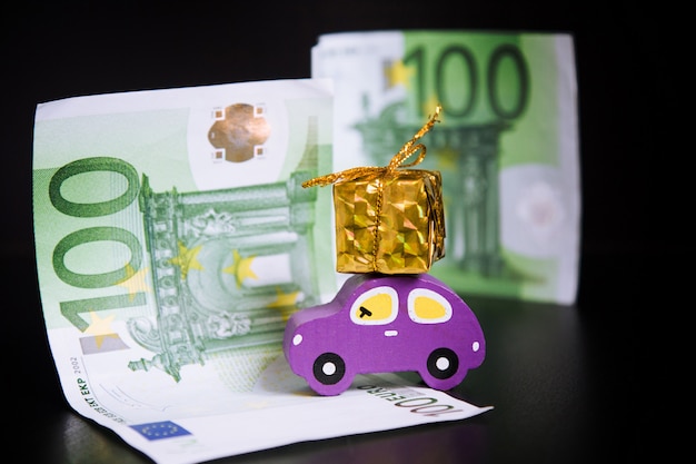 Игрушечный автомобиль, евро и золотой подарок на черном